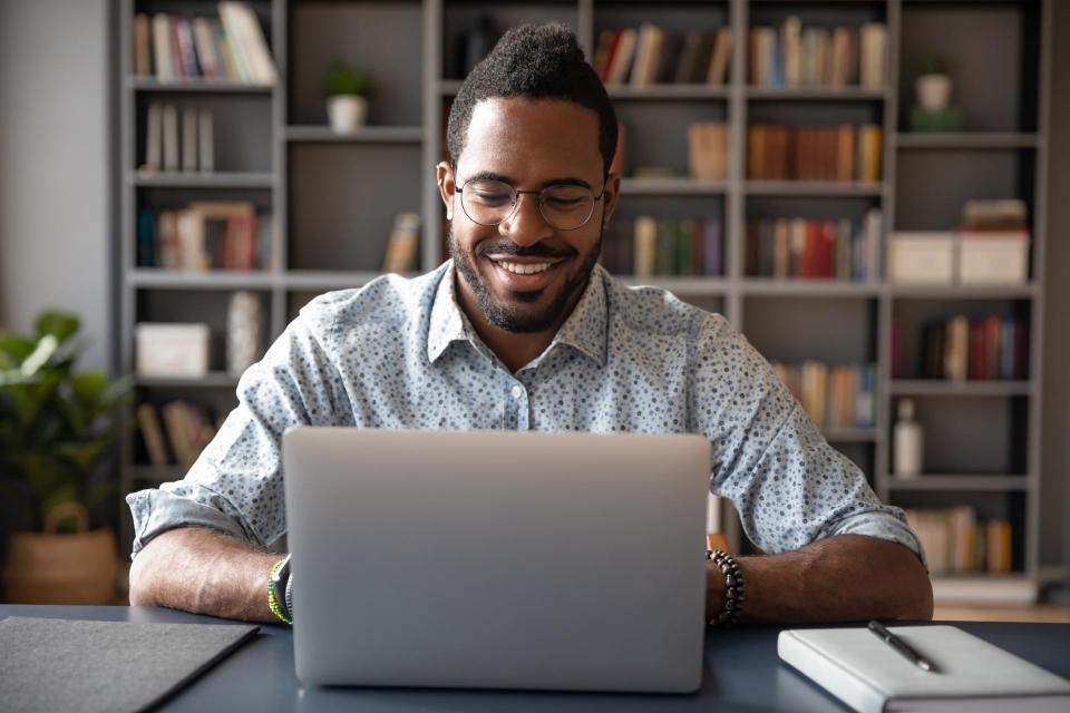 Front view head shot young smiling businessman in eyewear pleasantly looking at laptop screen