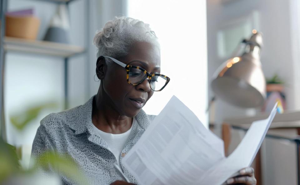 An elderly pretty African-American woman with glasses is looking through documents, business papers. Home office, budget planning, investments, taxes.