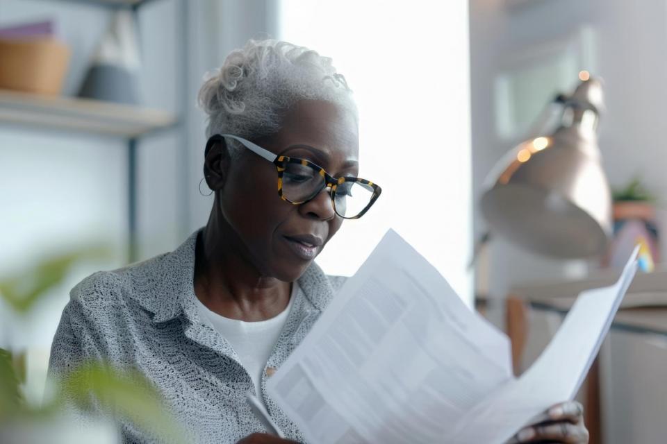 An elderly pretty African-American woman with glasses is looking through documents, business papers. Home office, budget planning, investments, taxes.